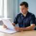 Agent public de sécurité en uniforme discret consultant des documents vierges à son bureau dans un environnement professionnel lumineux.