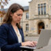 Une femme candidate à un poste de conseillère principale d’éducation relit attentivement un courriel sur un ordinateur portable devant un établissement scolaire français.